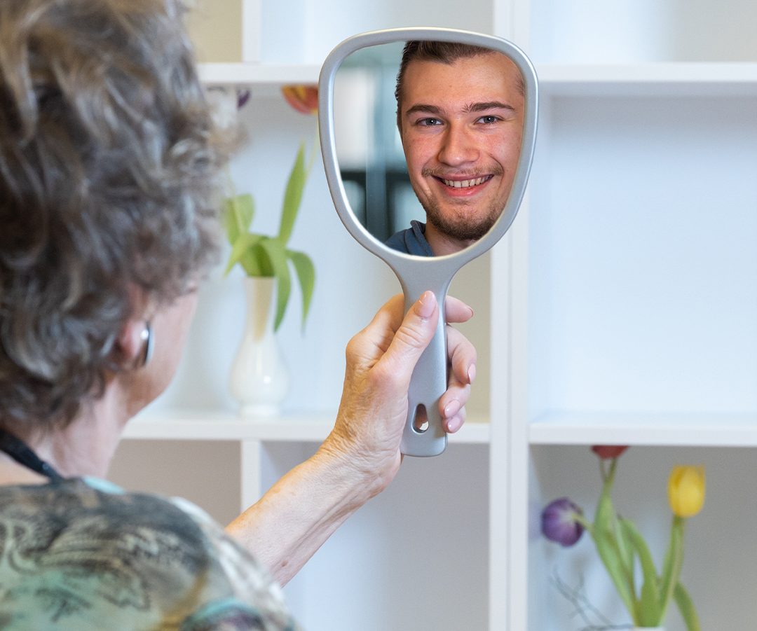 Ältere Person blickt in den Spiegel. Im Spiegelbild ist eine junge Person zu sehen.