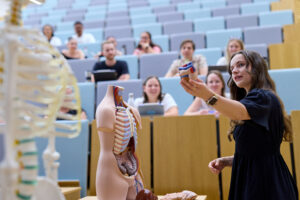 Eine Frau zeigt auf ein Skelett in einem Hörsaal für Studierende